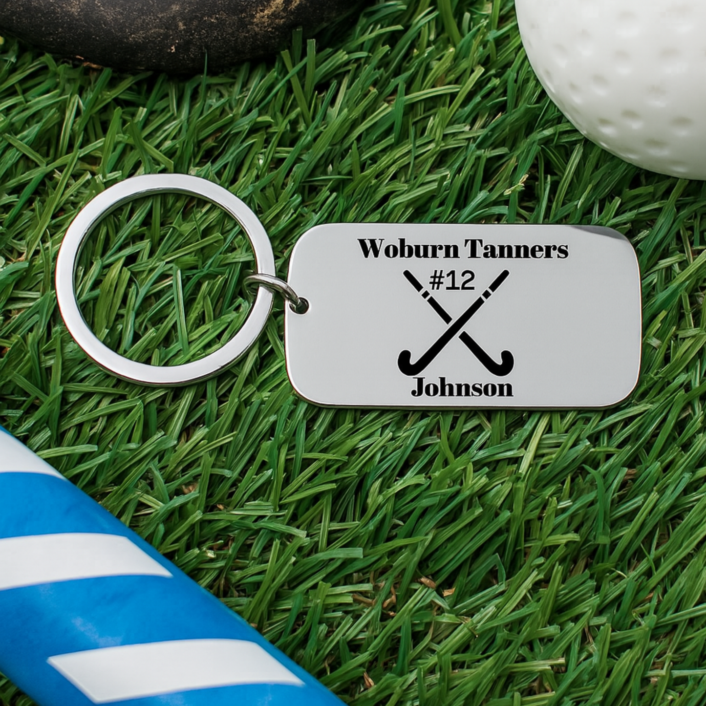 Engraved field hockey dog tag keychain placed on green artificial turf with hockey ball background