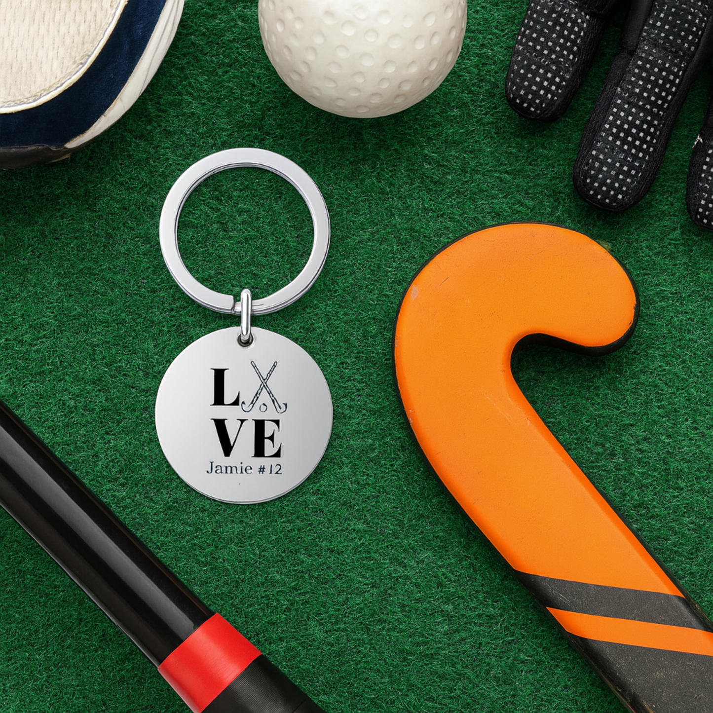 Field hockey LOVE keychain displayed on turf with orange and black sticks and ball