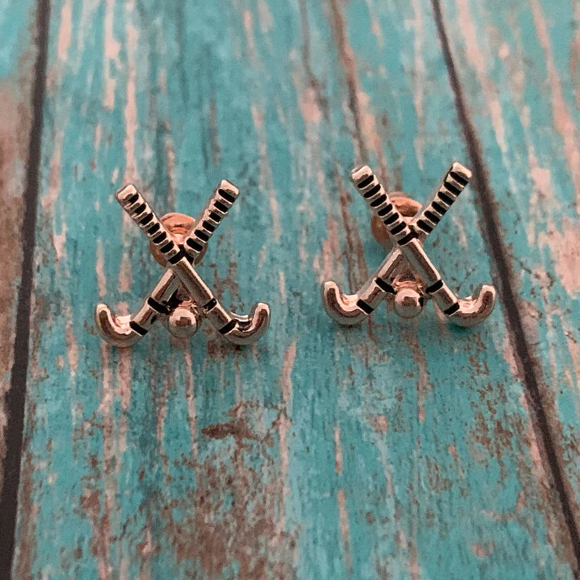 Rose gold field hockey earrings laid flat on rustic turquoise wood for stylish product photo