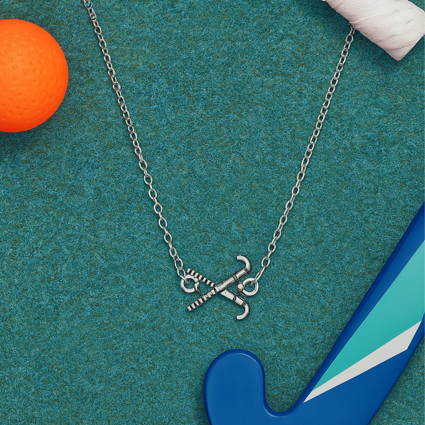 Field hockey charm necklace on teal background with orange ball and blue field hockey stick