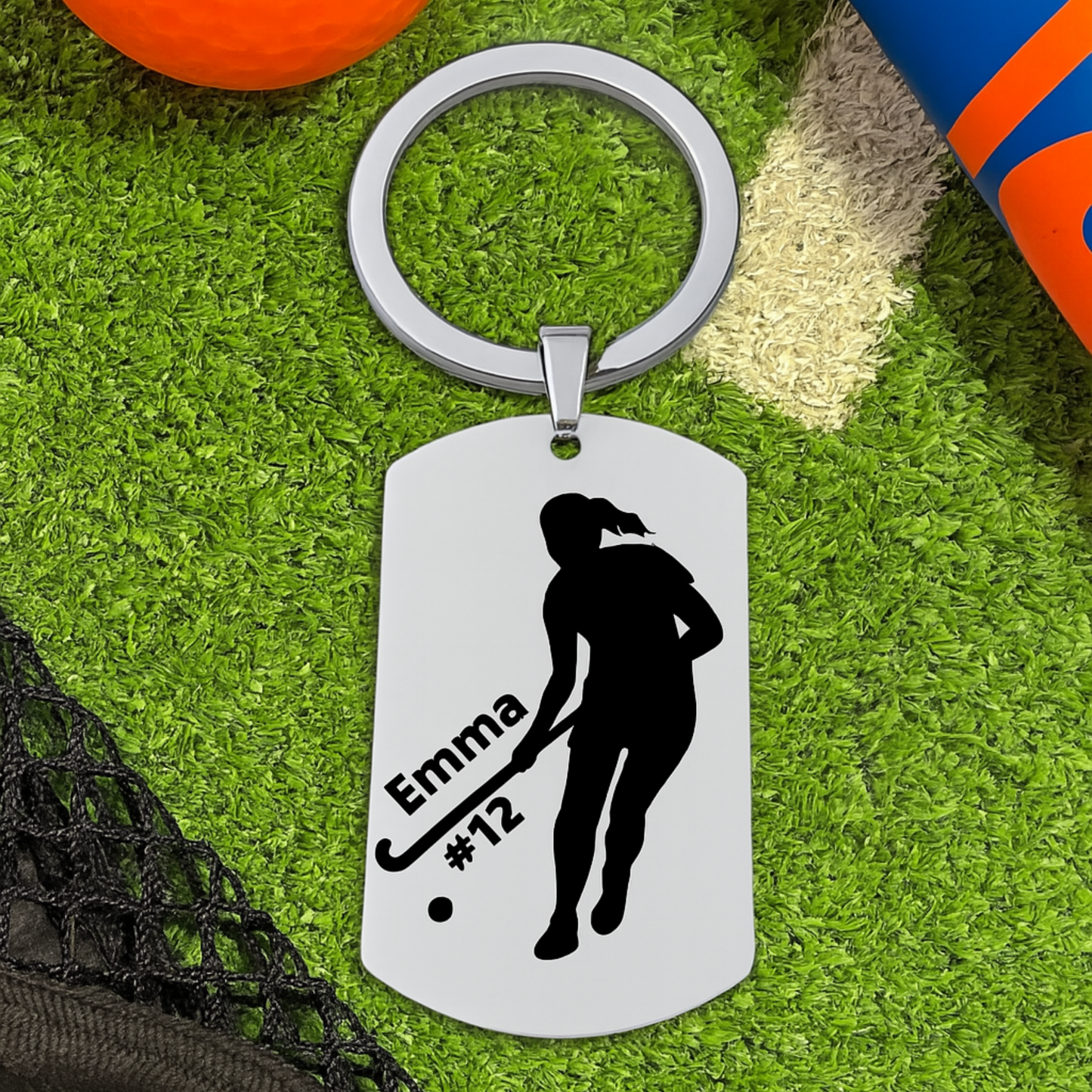 Personalized engraved field hockey player dog tag keychain on green artificial turf with hockey stick and ball