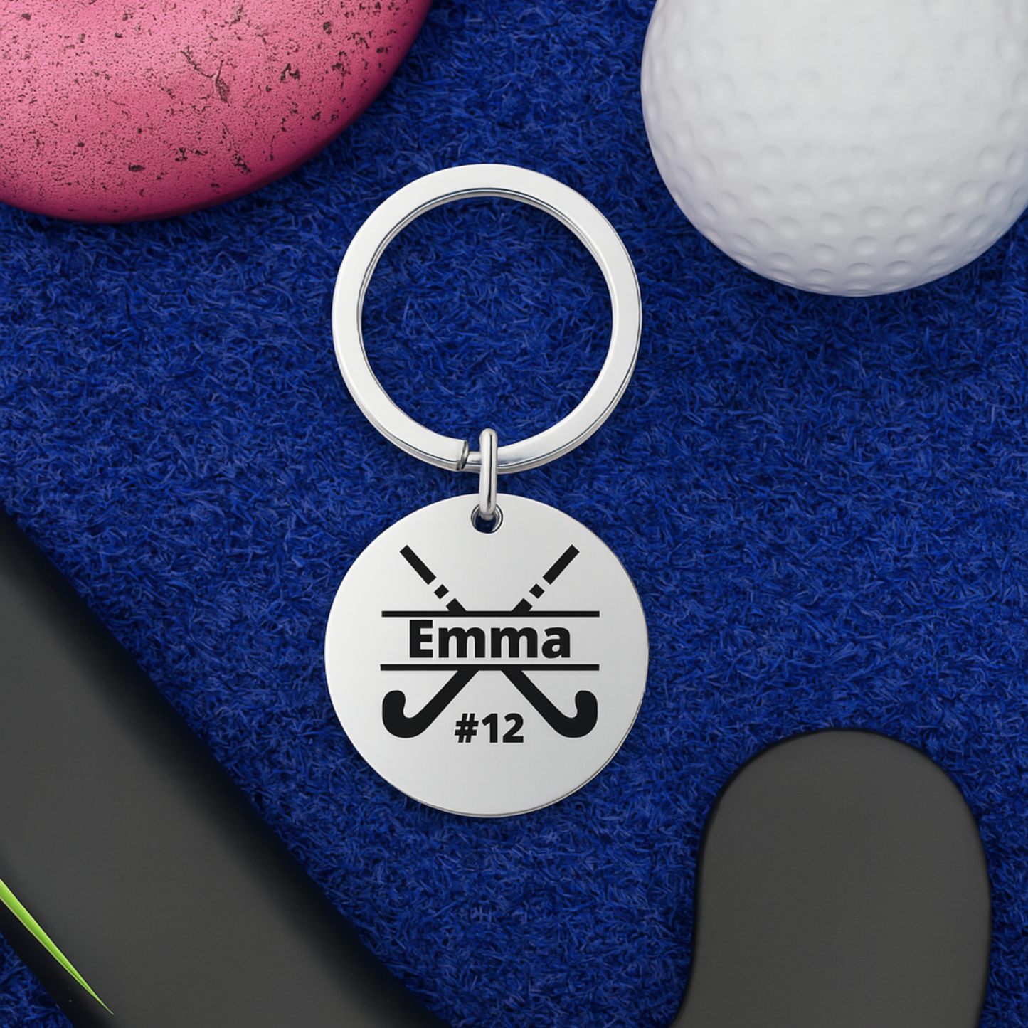 Engraved stainless steel field hockey stick keychain displayed on turf with sticks and ball