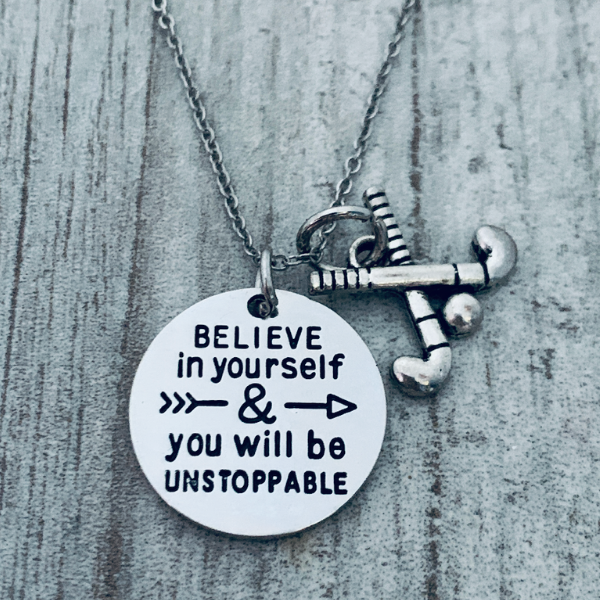 Silver motivational field hockey necklace displayed on textured gray background with disc and sticks