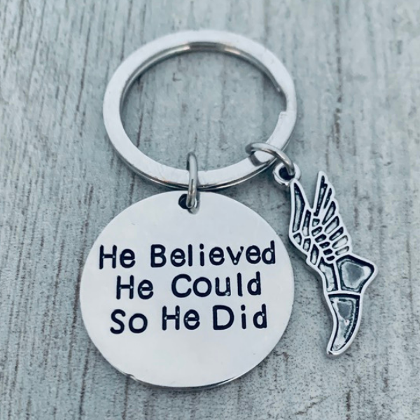 Detailed view of silver running shoe charm and 'He Believed He Could So He Did' disc on keyring