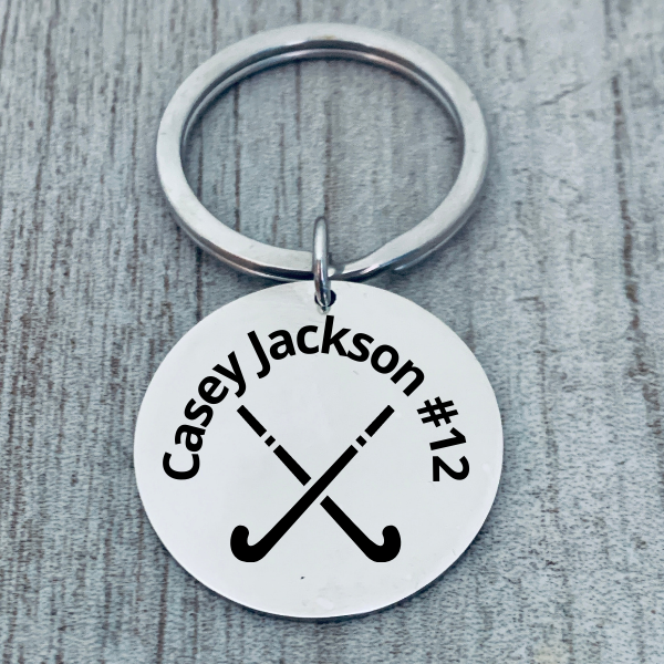 Close-up of name engraved stainless steel field hockey keychain on gray wood surface