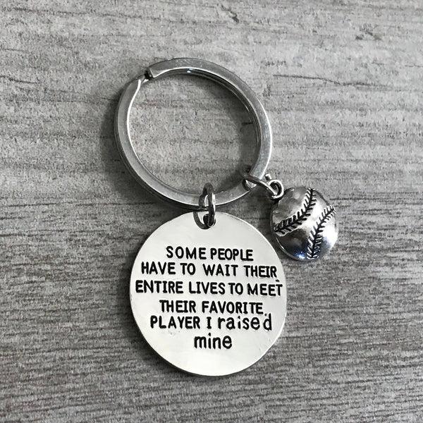 Inspirational softball keychain laid flat on wood surface, engraved charm in focus
