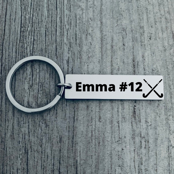Engraved field hockey bar keychain with personalized name and number displayed on wooden background