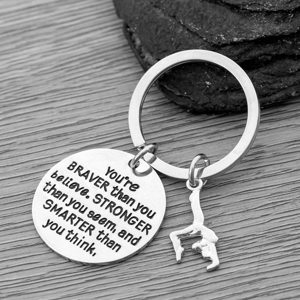 Silver-tone gymnast keychain with engraved disc and hanging charm, displayed on branding insert card for gift-giving
