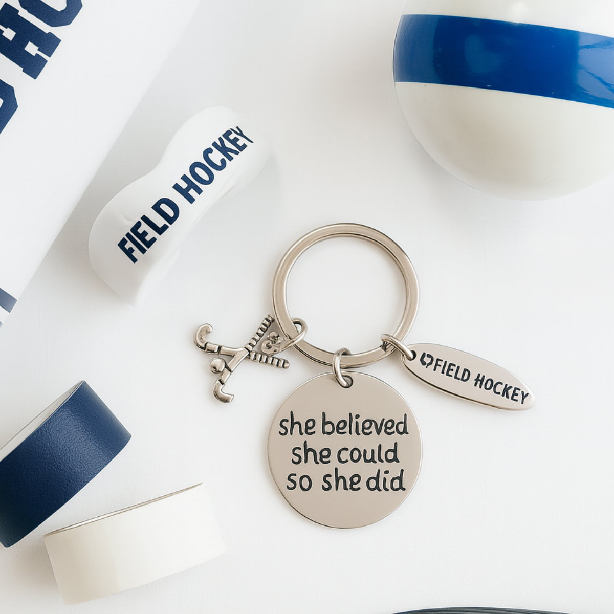 Inspirational field hockey keychain with She Believed She Could So She Did engraving displayed next to water bottle