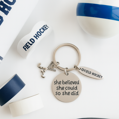 Inspirational field hockey keychain with She Believed She Could So She Did engraving displayed next to water bottle