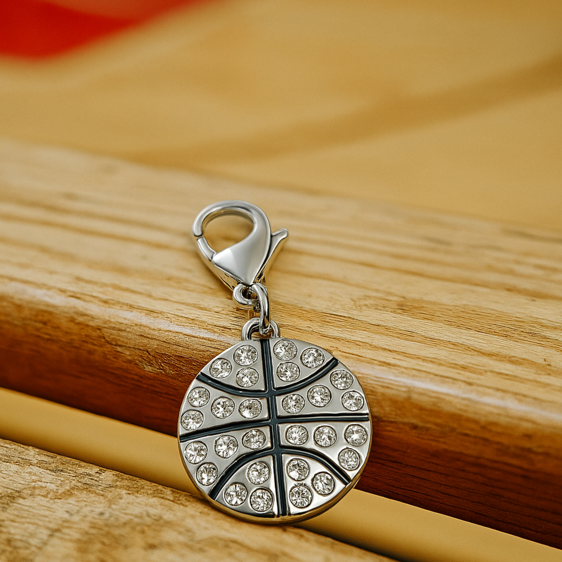 Flat-lay of basketball charm with lobster clasp resting on textured wood surface