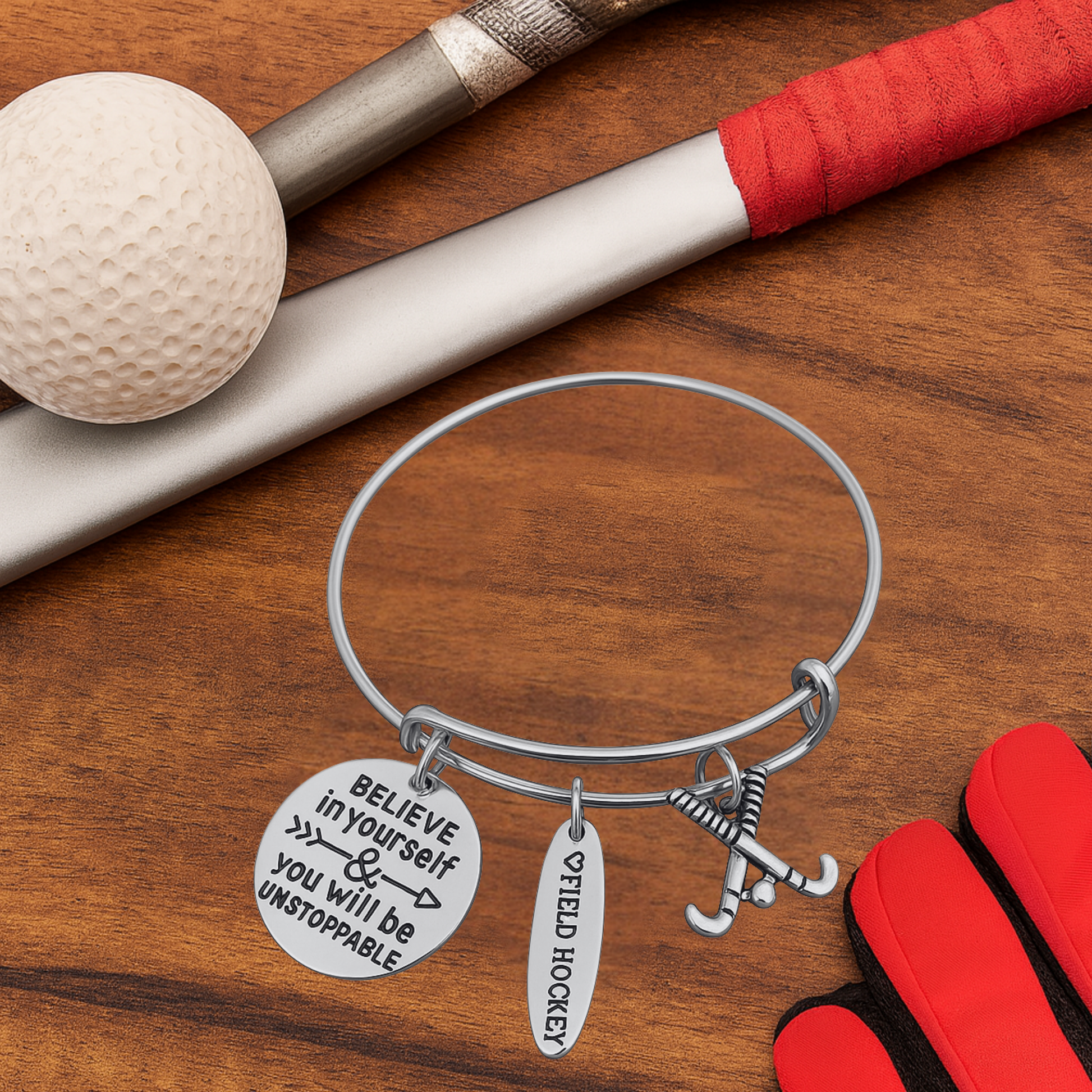 Inspirational field hockey charm bracelet displayed with field hockey sticks and ball