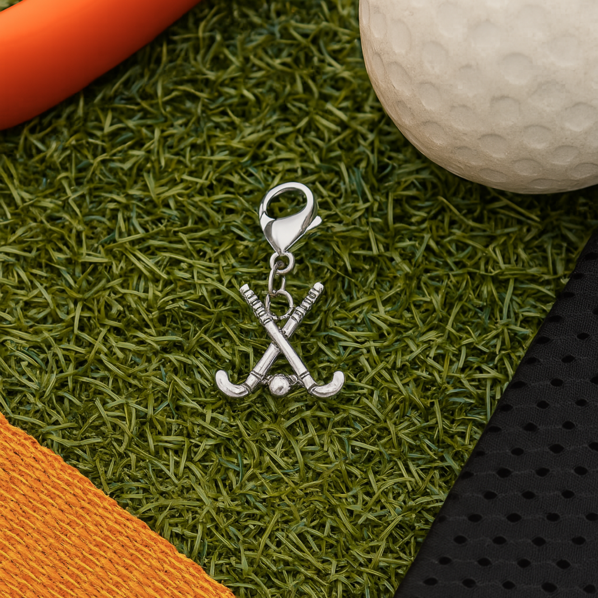 Field hockey zipper pull charm on artificial turf with hockey ball and stick background