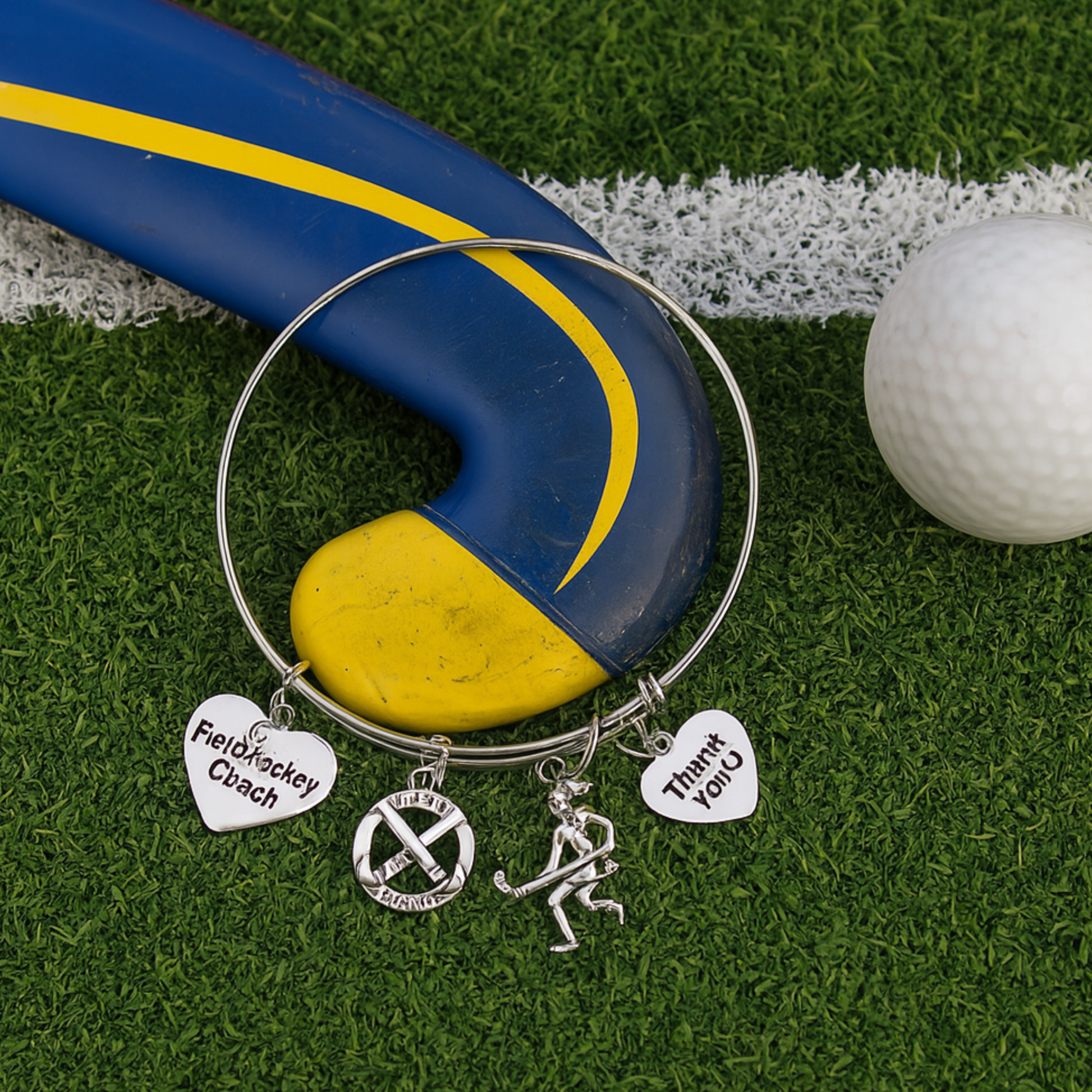 Field hockey coach charm bangle bracelet displayed on turf with yellow and white balls