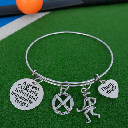 Silver coach bangle bracelet with field hockey charms displayed on green turf background
