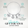 Adjustable silver coach bangle bracelet with engraved charms shown on turquoise background with product features