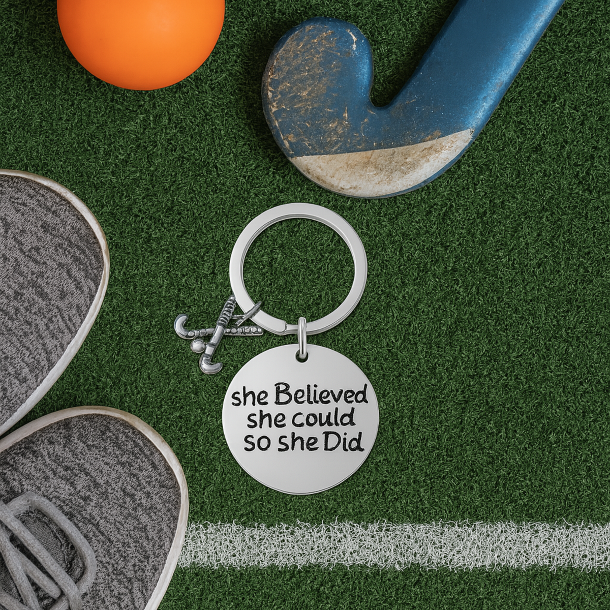 She Believed She Could So She Did field hockey keychain displayed on green artificial turf with hockey ball