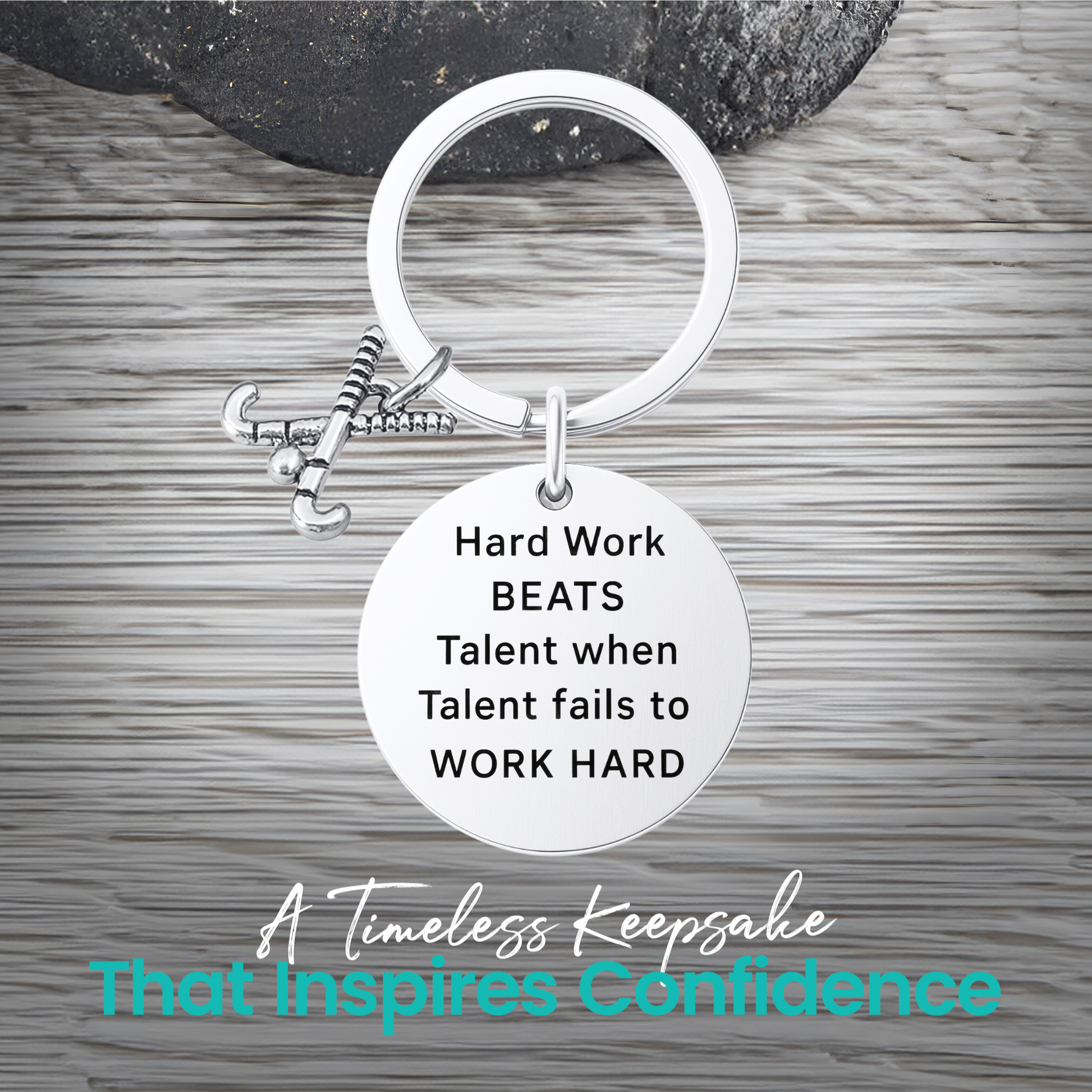 Silver field hockey keychain with engraved Work Hard Beats Talent charm on rustic wooden surface