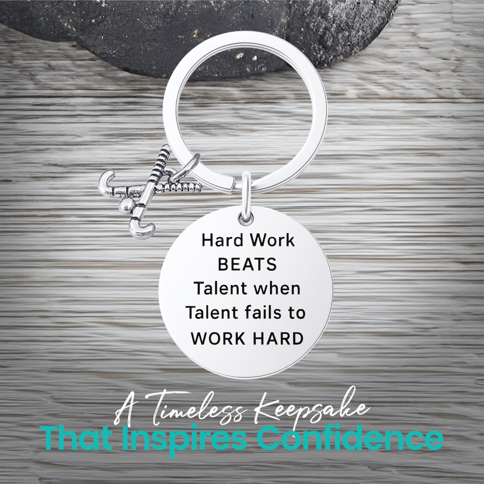 Silver field hockey keychain with engraved Work Hard Beats Talent charm on rustic wooden surface