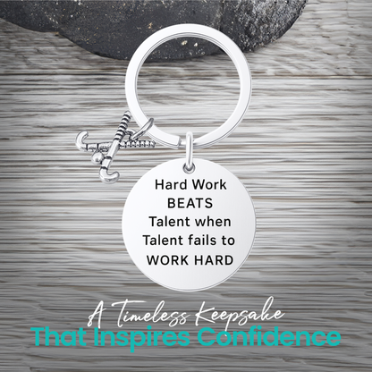Silver field hockey keychain with engraved Work Hard Beats Talent charm on rustic wooden surface