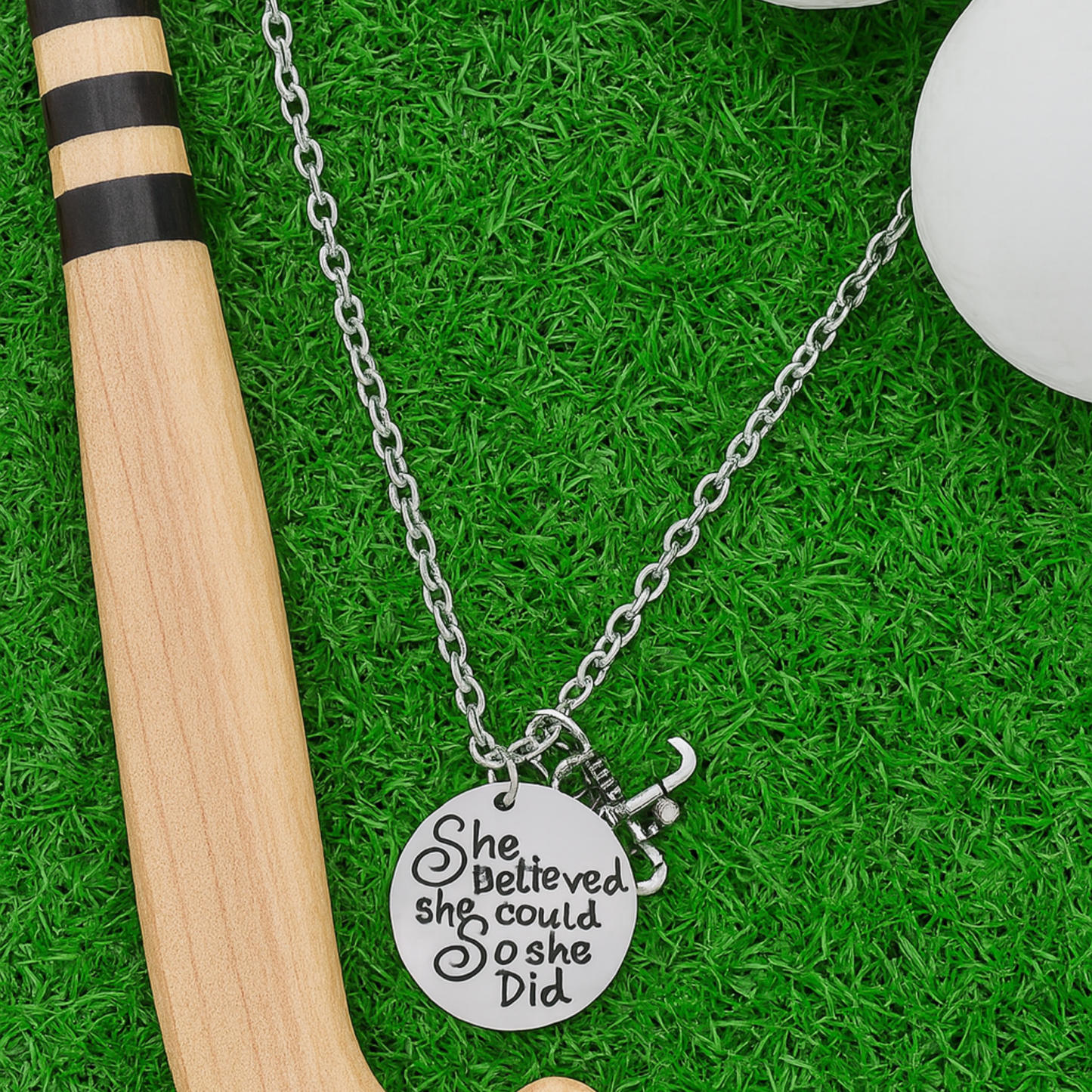Field hockey necklace with engraved inspirational quote displayed on artificial turf with hockey stick