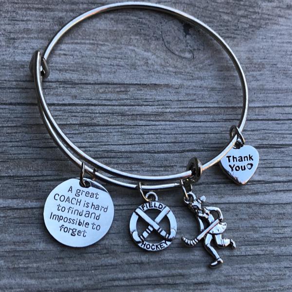 Close-up of field hockey coach bangle bracelet with charms displayed on wood surface
