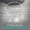 Expandable silver gymnastics bangle bracelet with charms displayed on rustic wooden surface