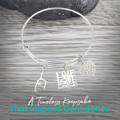 Expandable silver gymnastics bangle bracelet with charms displayed on rustic wooden surface