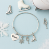 Figure skating coach charm bracelet with silver skater, snowflake, and heart charms arranged on white surface