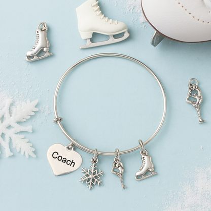 Figure skating coach charm bracelet with silver skater, snowflake, and heart charms arranged on white surface