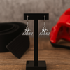 Close-up of “I Love Karate” earrings hanging on black display with red martial arts props in background