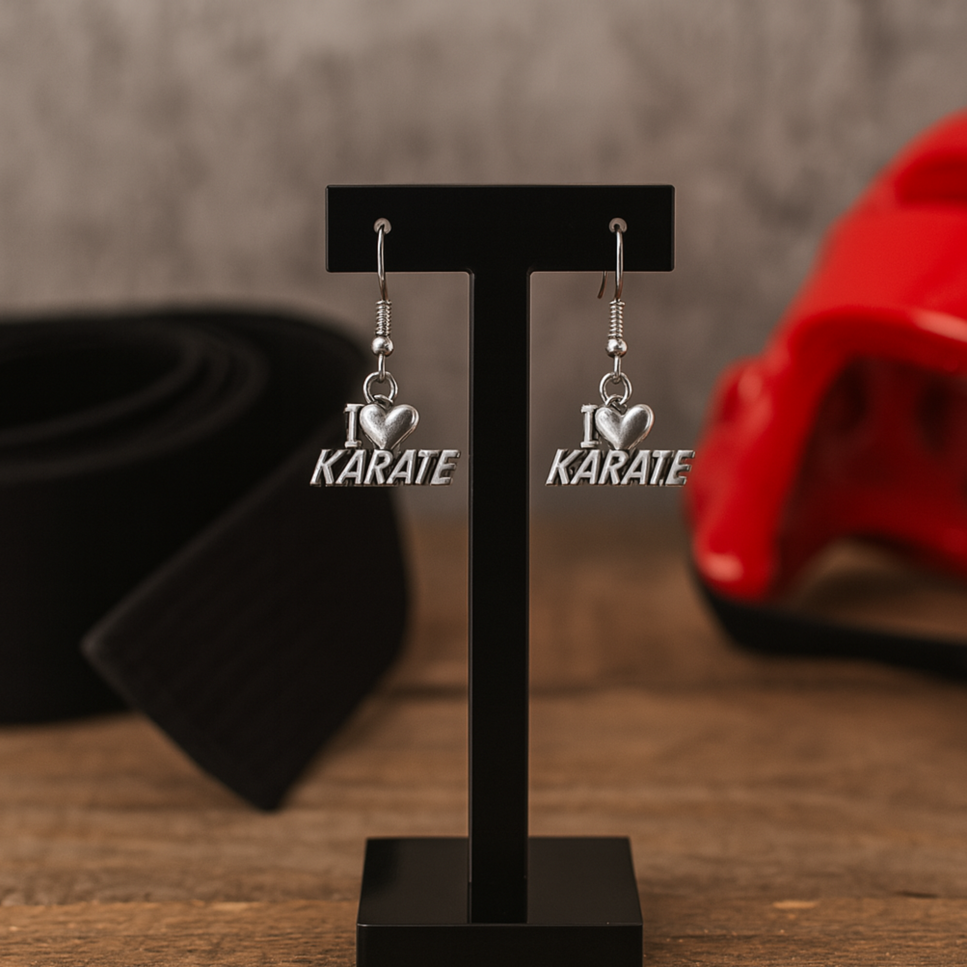 Close-up of “I Love Karate” earrings hanging on black display with red martial arts props in background