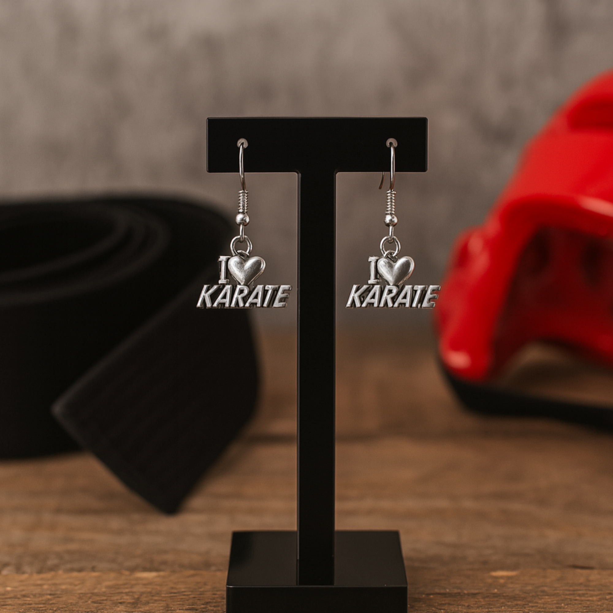 Close-up of “I Love Karate” earrings hanging on black display with red martial arts props in background