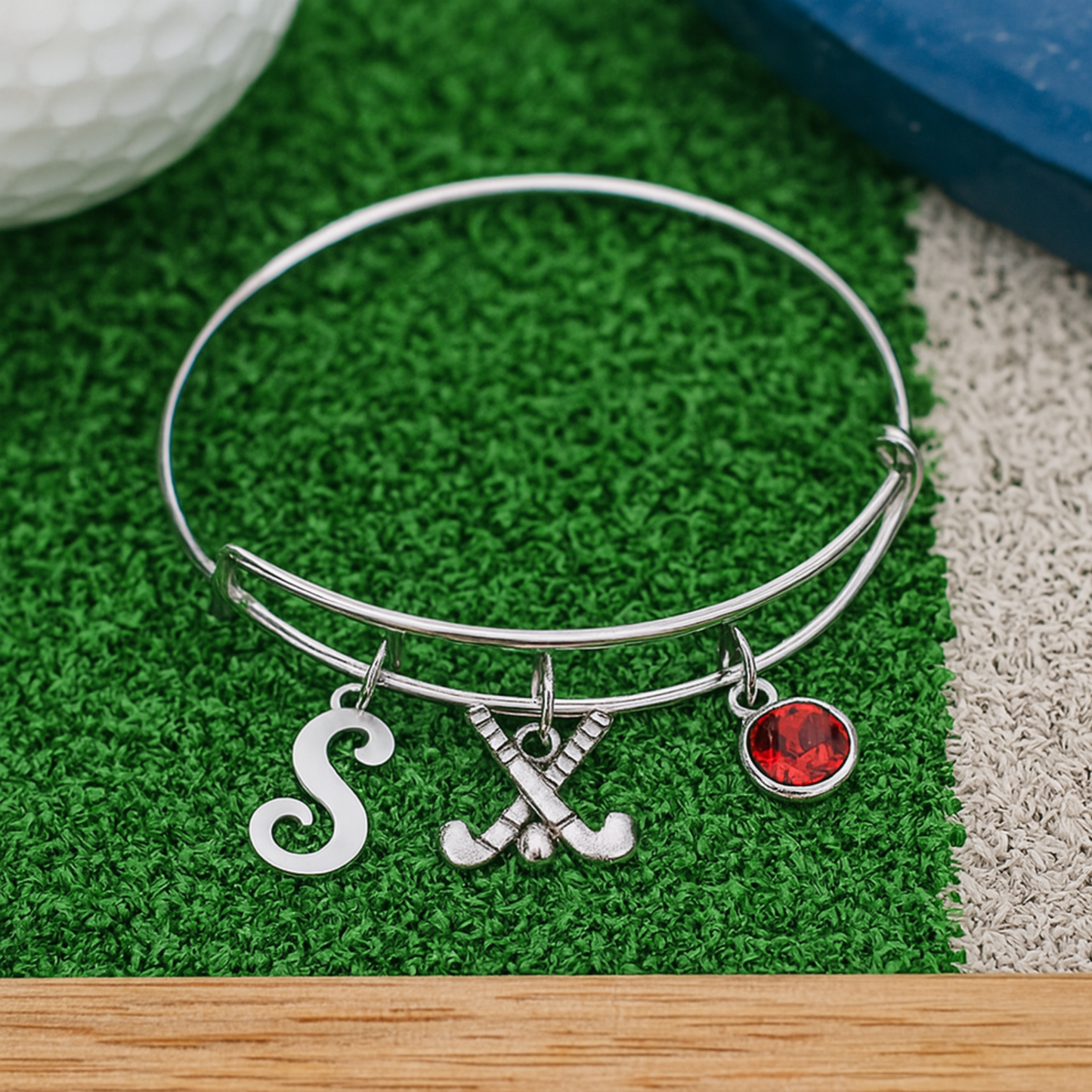 Personalized field hockey bangle bracelet with letter and birthstone charms displayed on artificial turf
