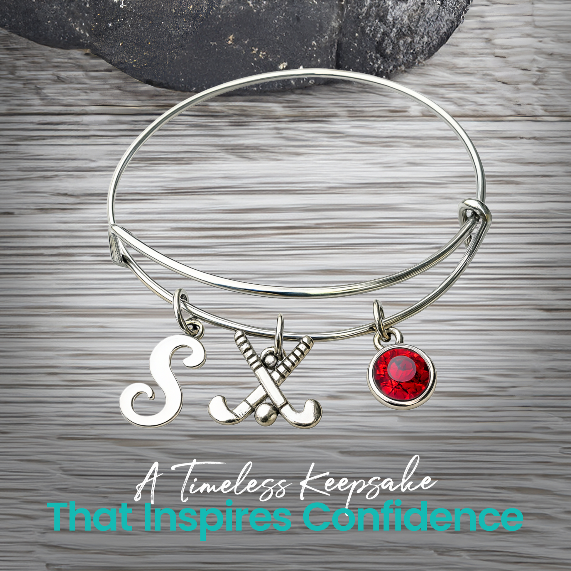 Silver adjustable field hockey bangle bracelet with personalized letter charm and red birthstone on rustic wood