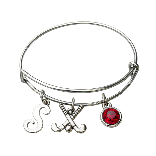 Adjustable silver field hockey bangle bracelet with letter charm, crossed sticks charm, and red birthstone charm