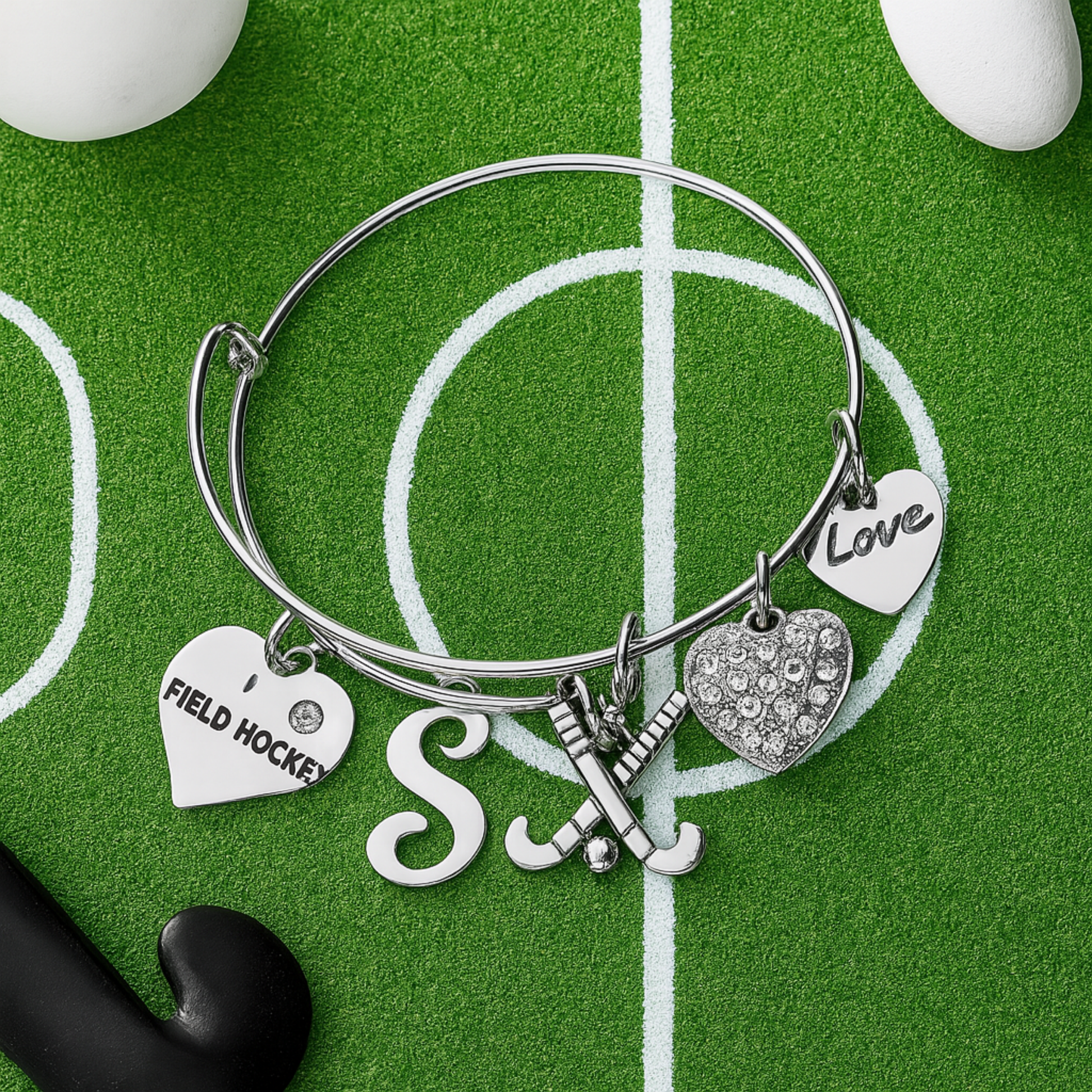Field hockey bangle bracelet with letter charm displayed on green artificial turf with ball
