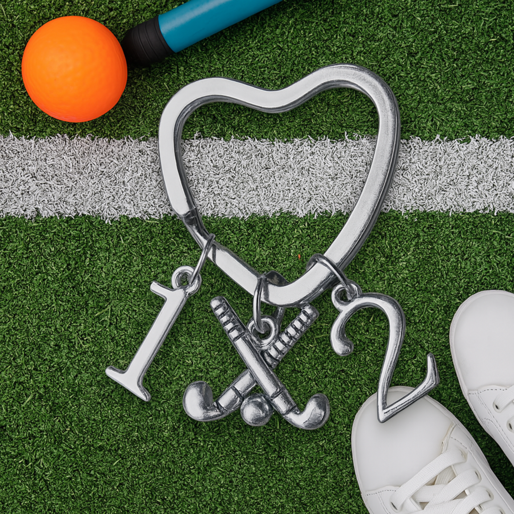 Heart-shaped field hockey keychain with number charms displayed on green artificial turf with hockey ball