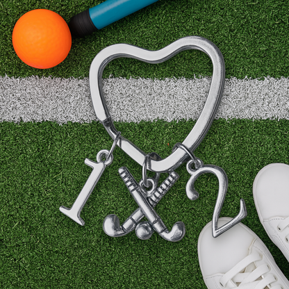 Heart-shaped field hockey keychain with number charms displayed on green artificial turf with hockey ball