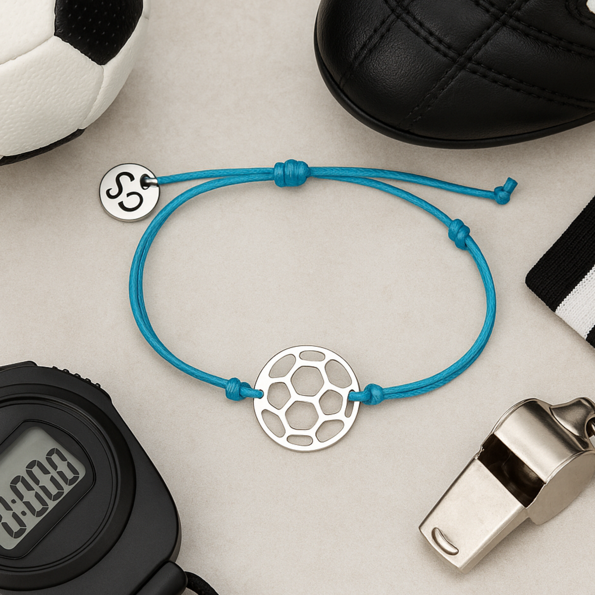 Blue adjustable soccer bracelet with stainless steel charm displayed with sports gear