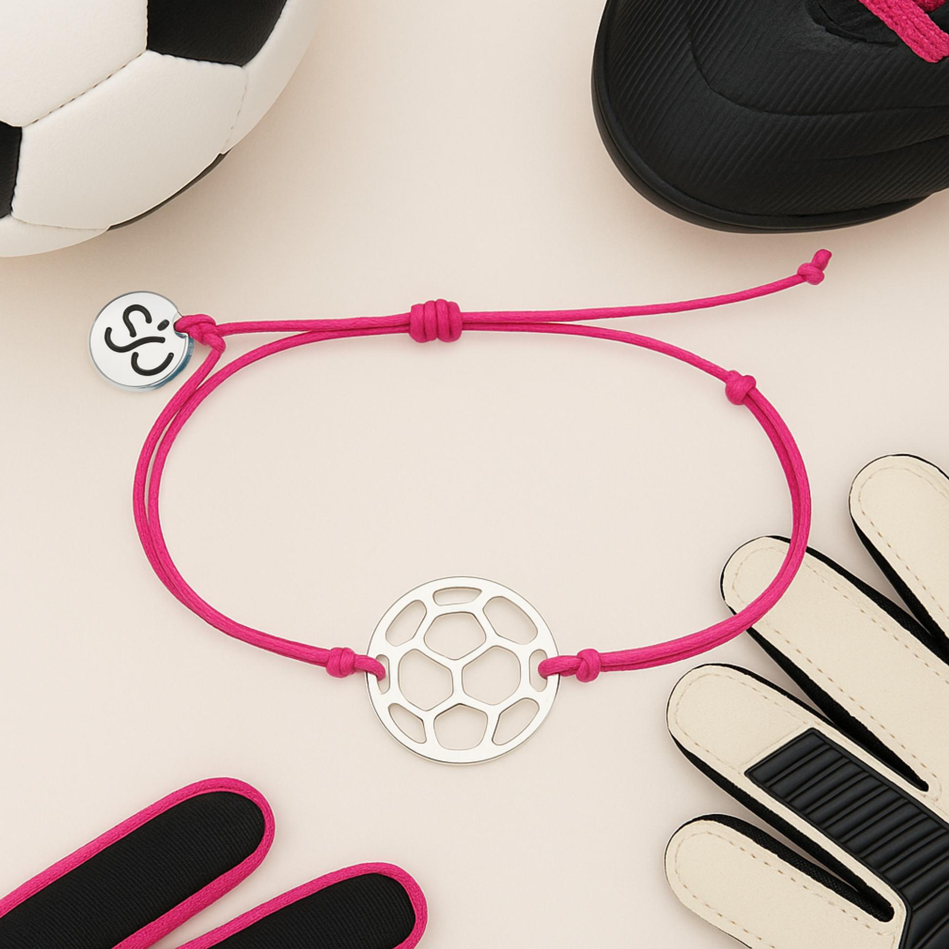 Pink soccer charm bracelet with stainless steel ball charm shown with soccer equipment