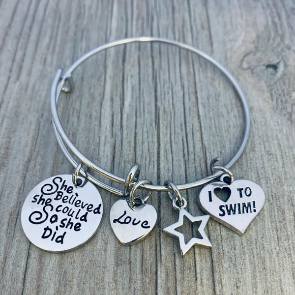 Motivational girls swimming bracelet with silver charms displayed on rustic wooden background