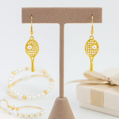 Gold tennis racket pearl dangle earrings displayed on jewelry stand