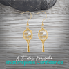 Gold tennis racket pearl earrings styled on rustic background