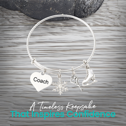 Figure skating bangle bracelet with coach heart charm displayed on rustic gray wooden surface