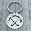Close-up of name engraved stainless steel field hockey keychain on gray wood surface
