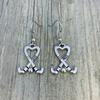 Silver heart-shaped field hockey stick earrings with crossed sticks displayed on rustic wooden surface