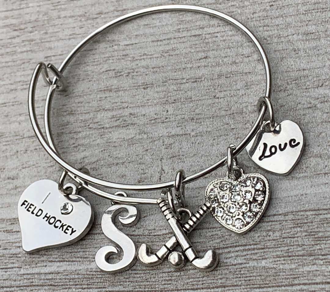 Personalized silver field hockey bangle bracelet with letter charm and heart charms on rustic wood surface