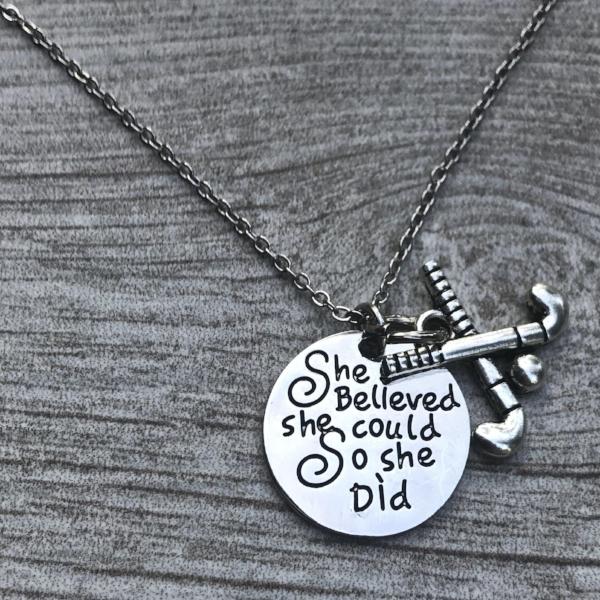 Silver field hockey necklace with engraved inspirational pendant displayed on gray fabric