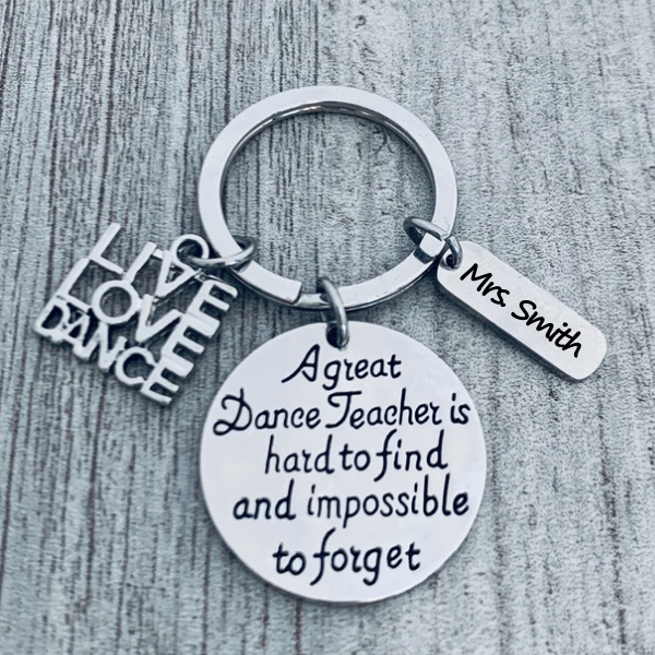 Dance-themed keychain with silver-tone charms shown on fabric background